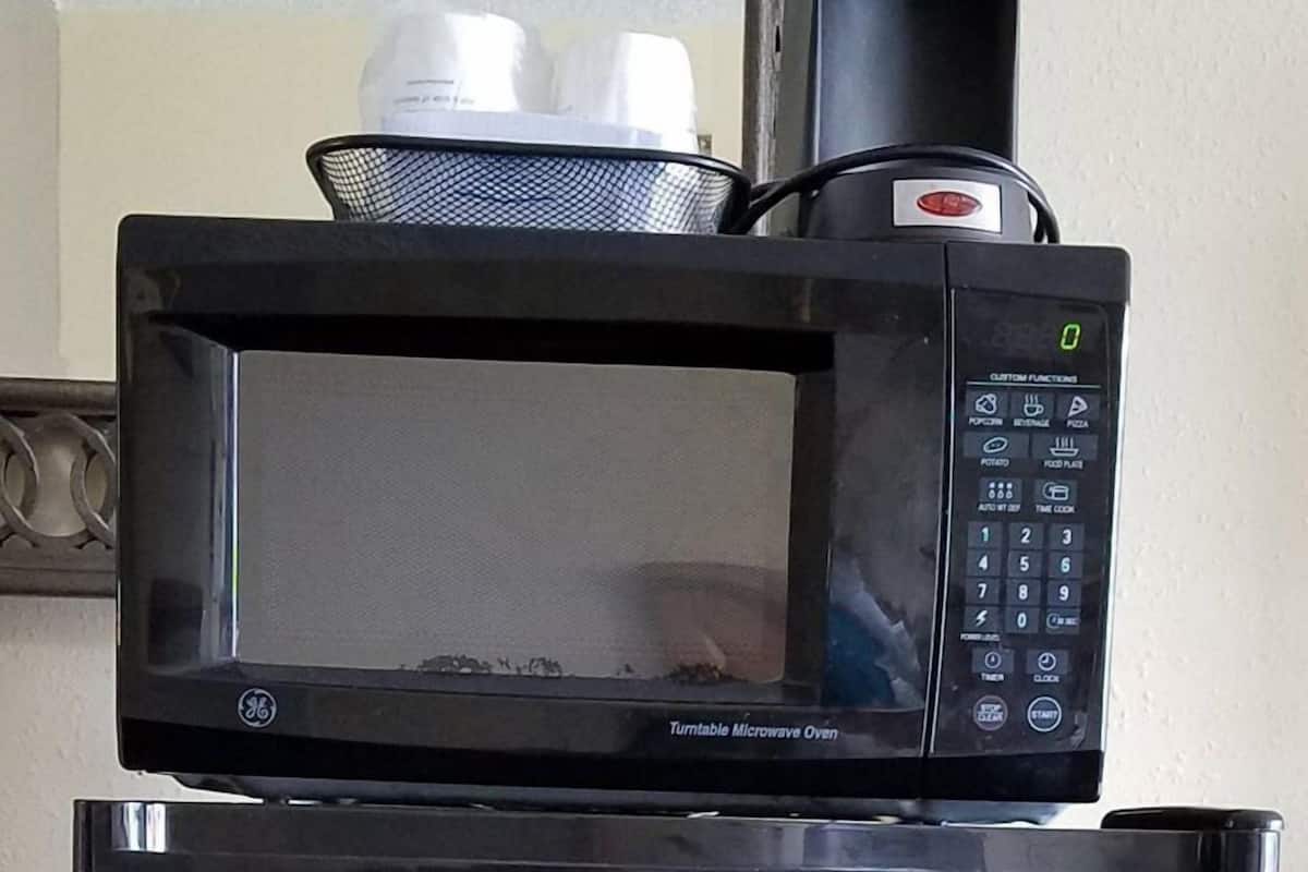 Un réfrigérateur noir avec un four à micro-ondes placé sur le dessus, le logo « LodgingStar » et une étiquette indiquant « Four à micro-ondes à plateau tournant ».