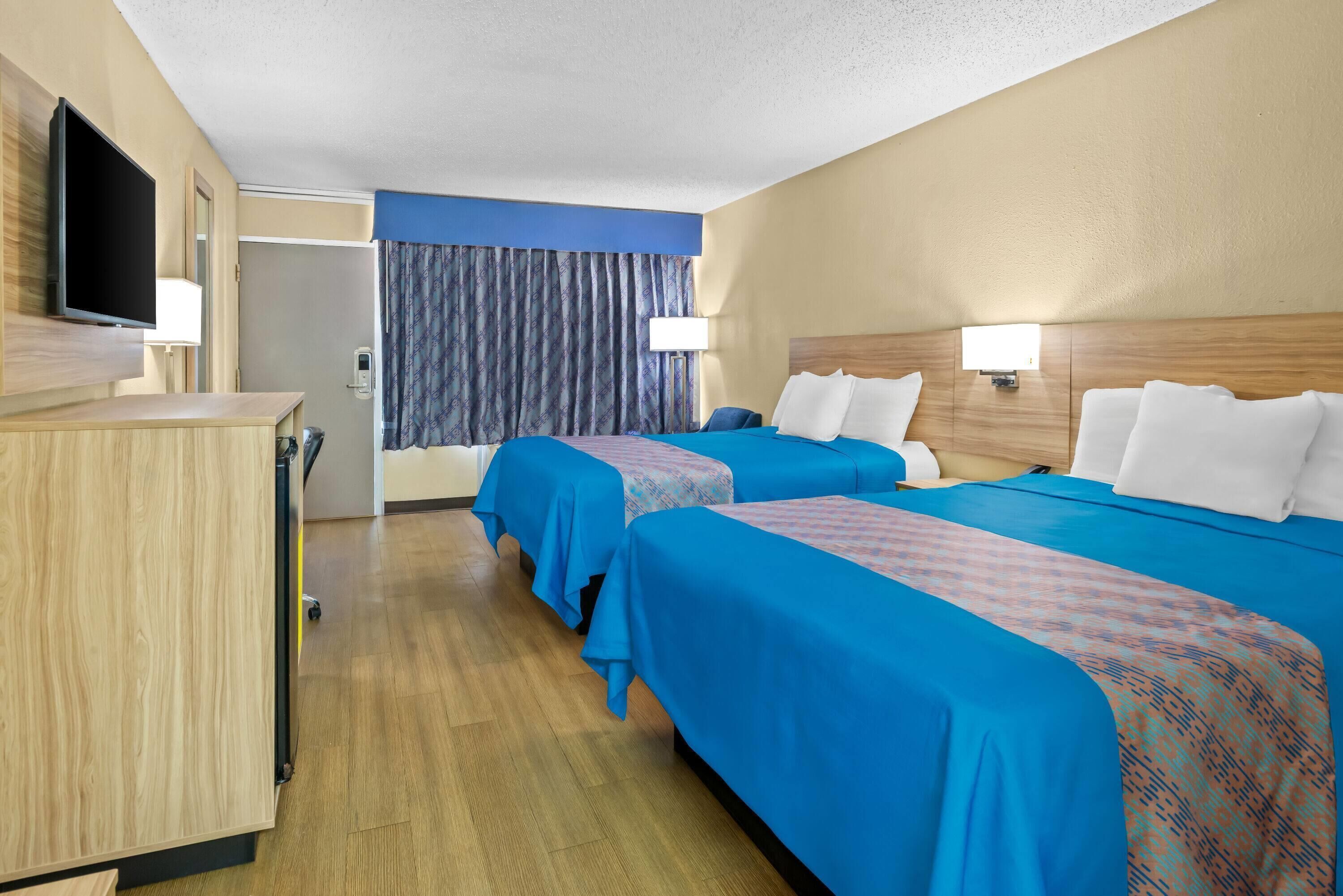 Habitación de hotel con dos camas, un escritorio, un televisor y la puerta del baño.
