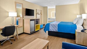 Habitación de hotel con cama, escritorio, silla, televisor y una pequeña cocina.