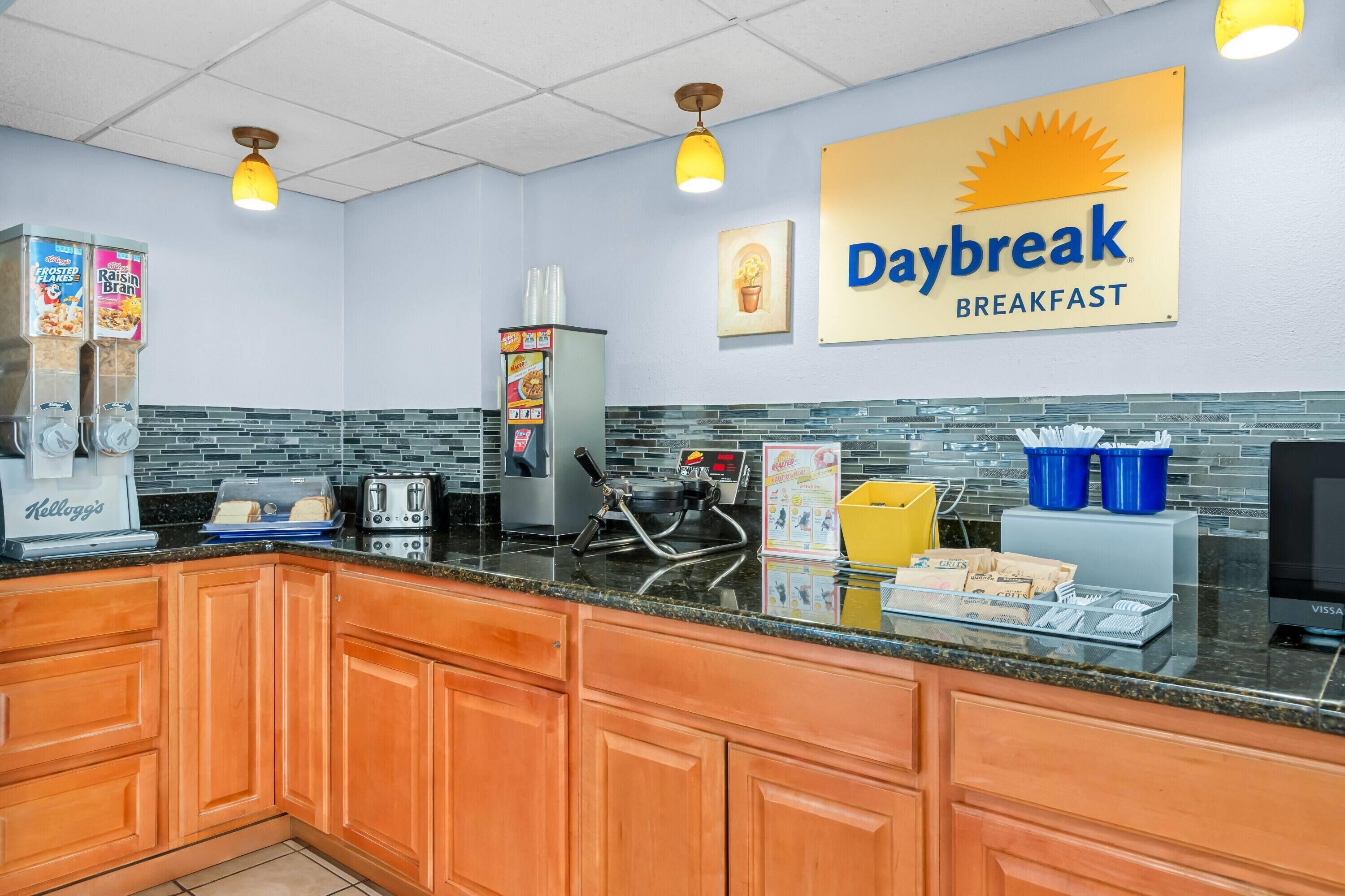 Un área de desayuno con un letrero que dice "Daybreak Breakfast", una cafetera, un tostador y un refrigerador.