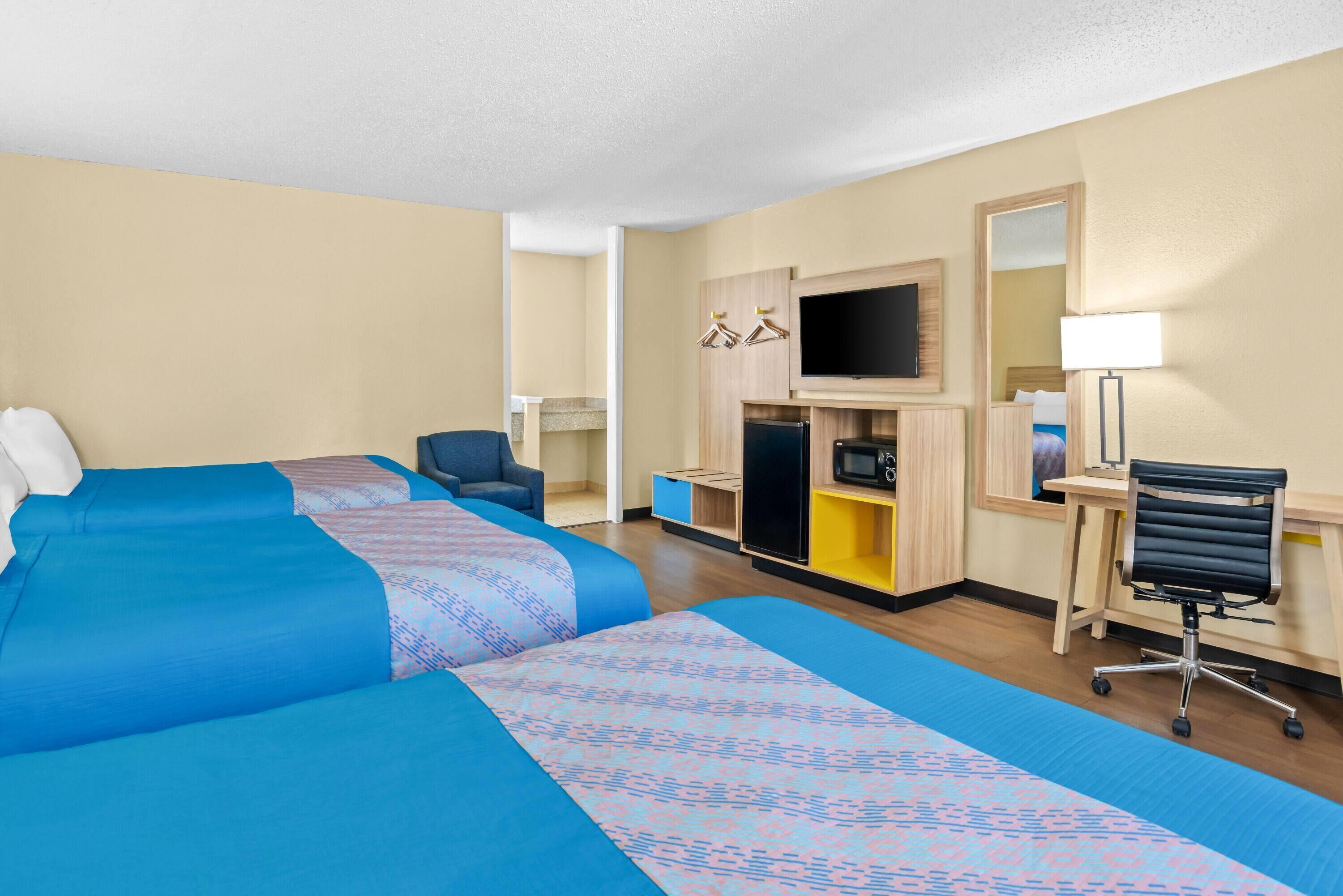 A hotel room with two large beds, a desk, a chair, a TV, and a microwave.