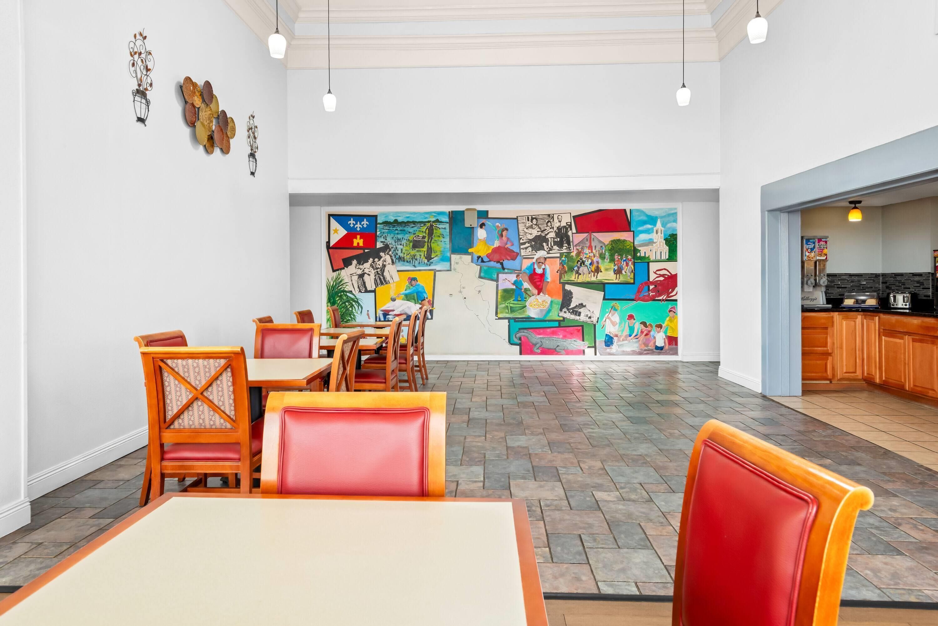 A dining area with wooden tables and chairs, a colorful mural on the wall, and a kitchen visible through an open doorway.