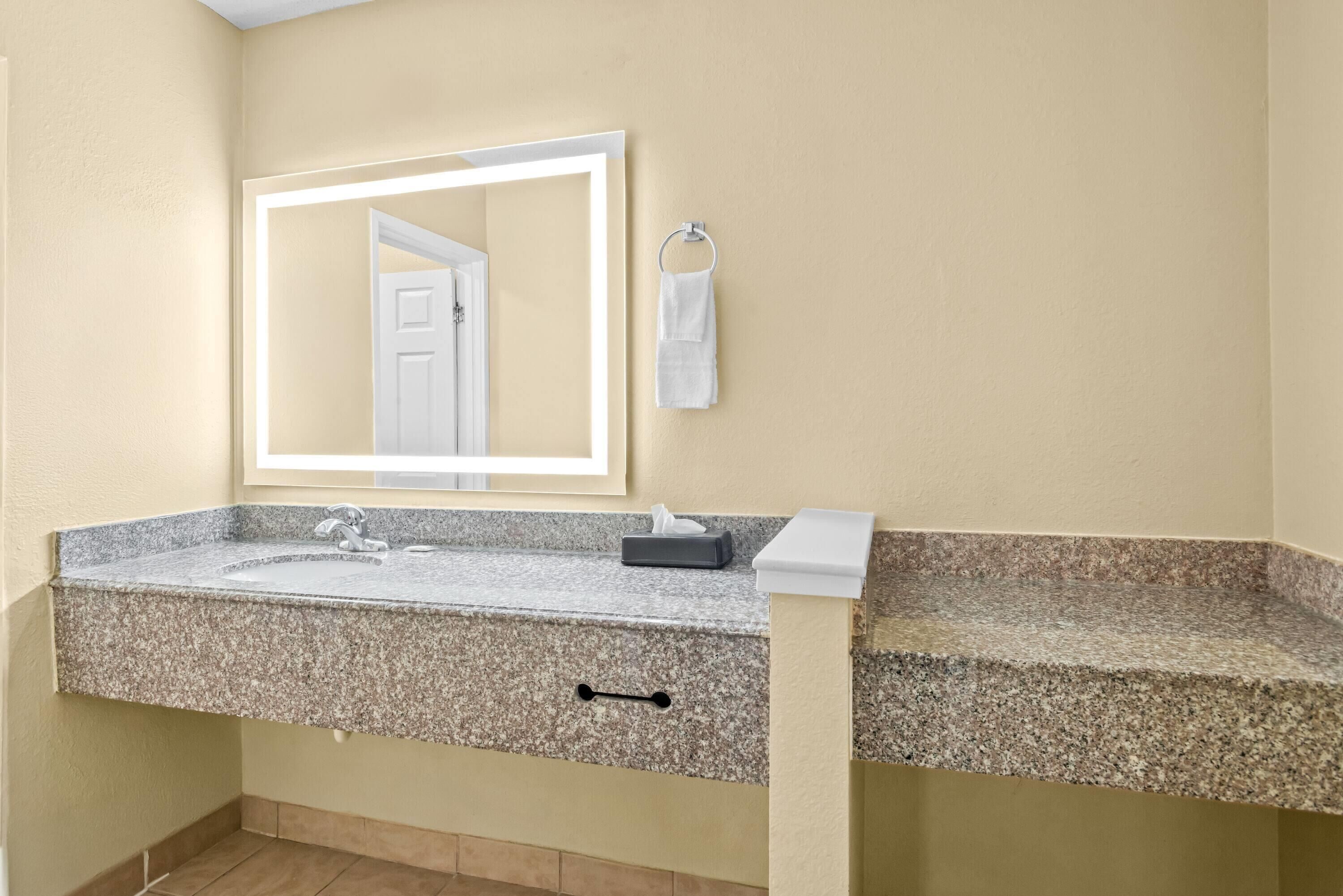 A bathroom with a granite countertop, a mirror, a towel rack, and a tissue box.