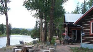 A rustic cabin with a gravel patio, outdoor seating, and a view of a lake. - Riverside Meadows Cabins (South Fork)