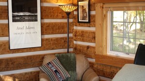 A cozy cabin room with a bed, a chair, a lamp, and framed pictures on the wall. - Riverside Meadows Cabins (South Fork)