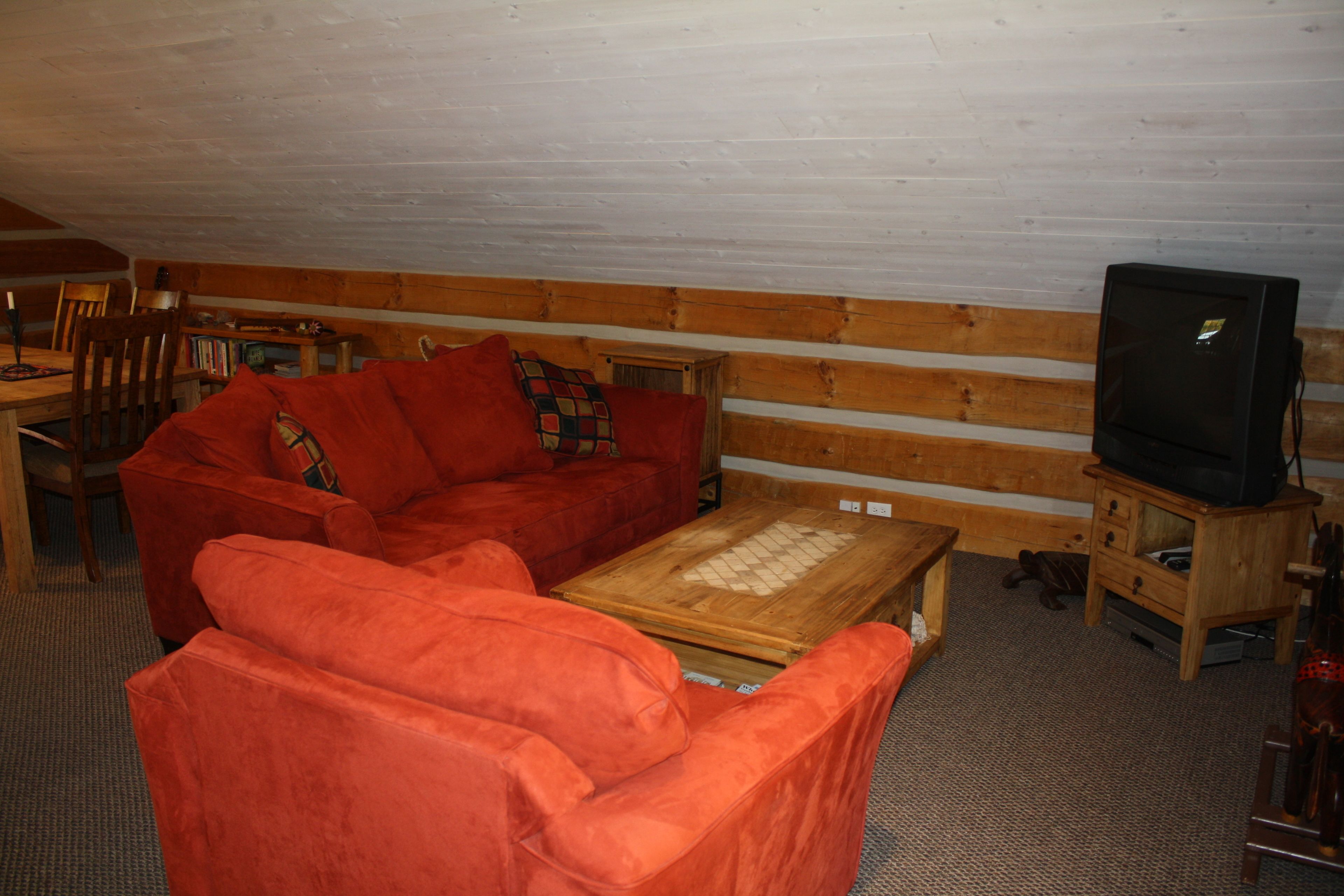 Un salon chaleureux avec un canapé rouge, une table basse en bois et un téléviseur posé sur un meuble en bois.