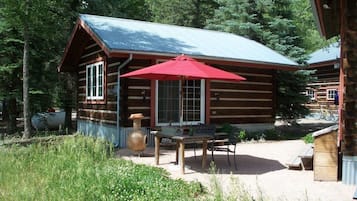 A rustic log cabin with a red umbrella, a wooden table, and a bench.