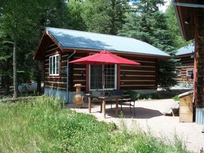 A rustic log cabin with a red umbrella, a wooden table, and a bench.