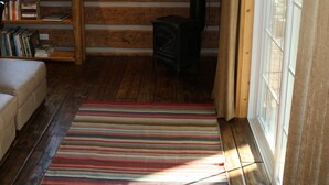 A log cabin interior with a sofa, a TV, a fireplace, and a window with curtains. - Riverside Meadows Cabins (South Fork)