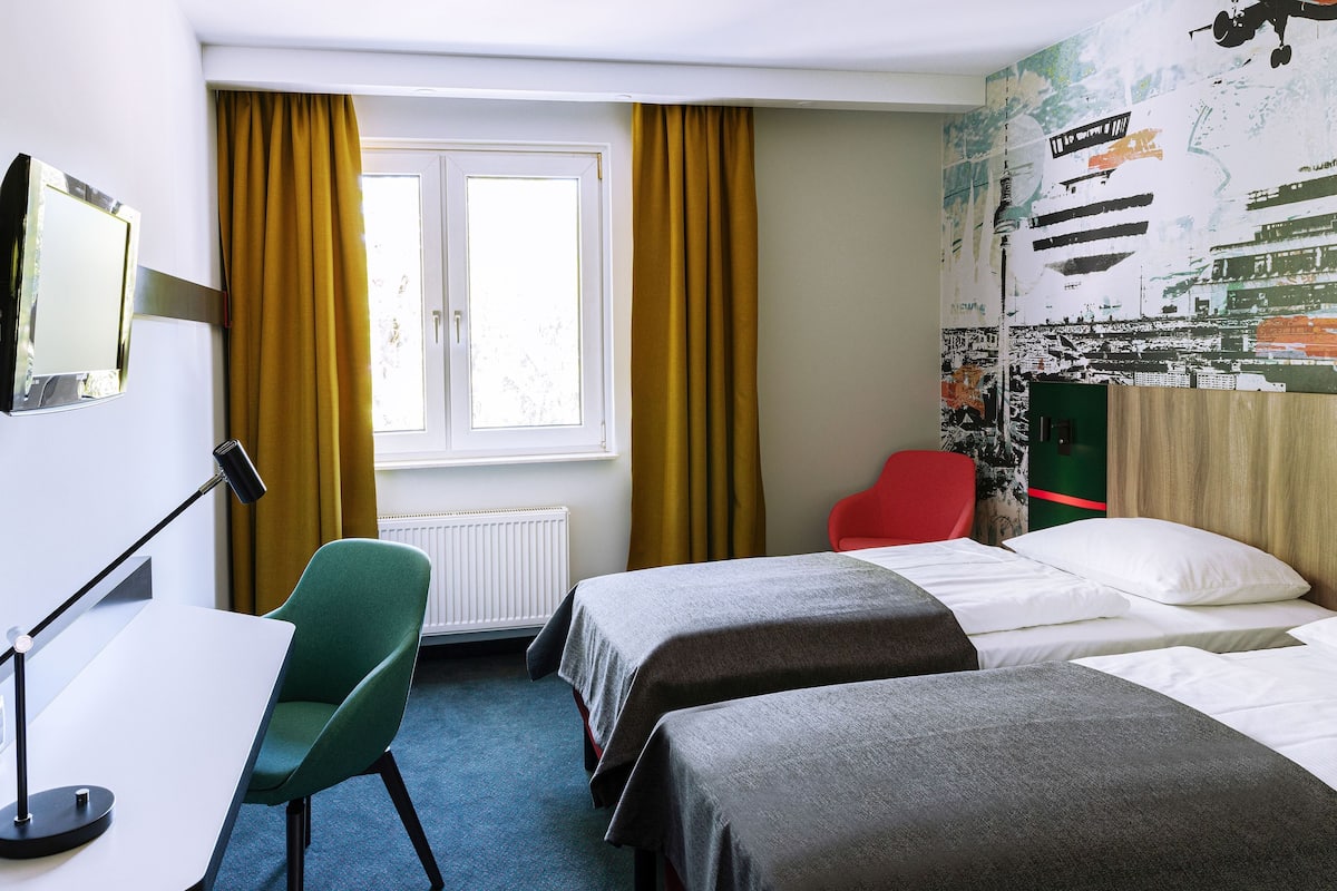 A hotel room with two beds, a desk, a chair, and a window with curtains.