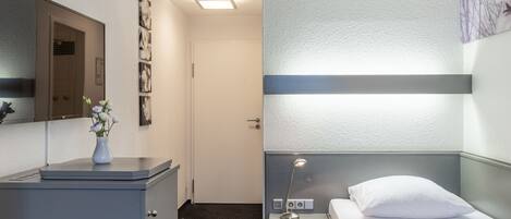 Una habitación de hotel con cama, mesita de noche, lámpara y un armario pequeño.