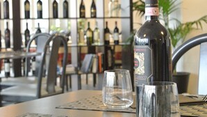 Une bouteille de vin est posée sur une table, accompagnée de deux verres, dans une pièce où l’on aperçoit un meuble à vin en arrière-plan.