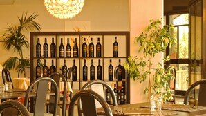 Un coin repas avec une table dressée pour quatre personnes, entourée de chaises, et un mur derrière recouvert de bouteilles de vin.