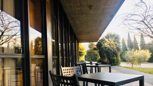 Un espace extérieur aménagé en terrasse, avec des tables et des chaises, de grandes fenêtres et une vue sur la verdure environnante.