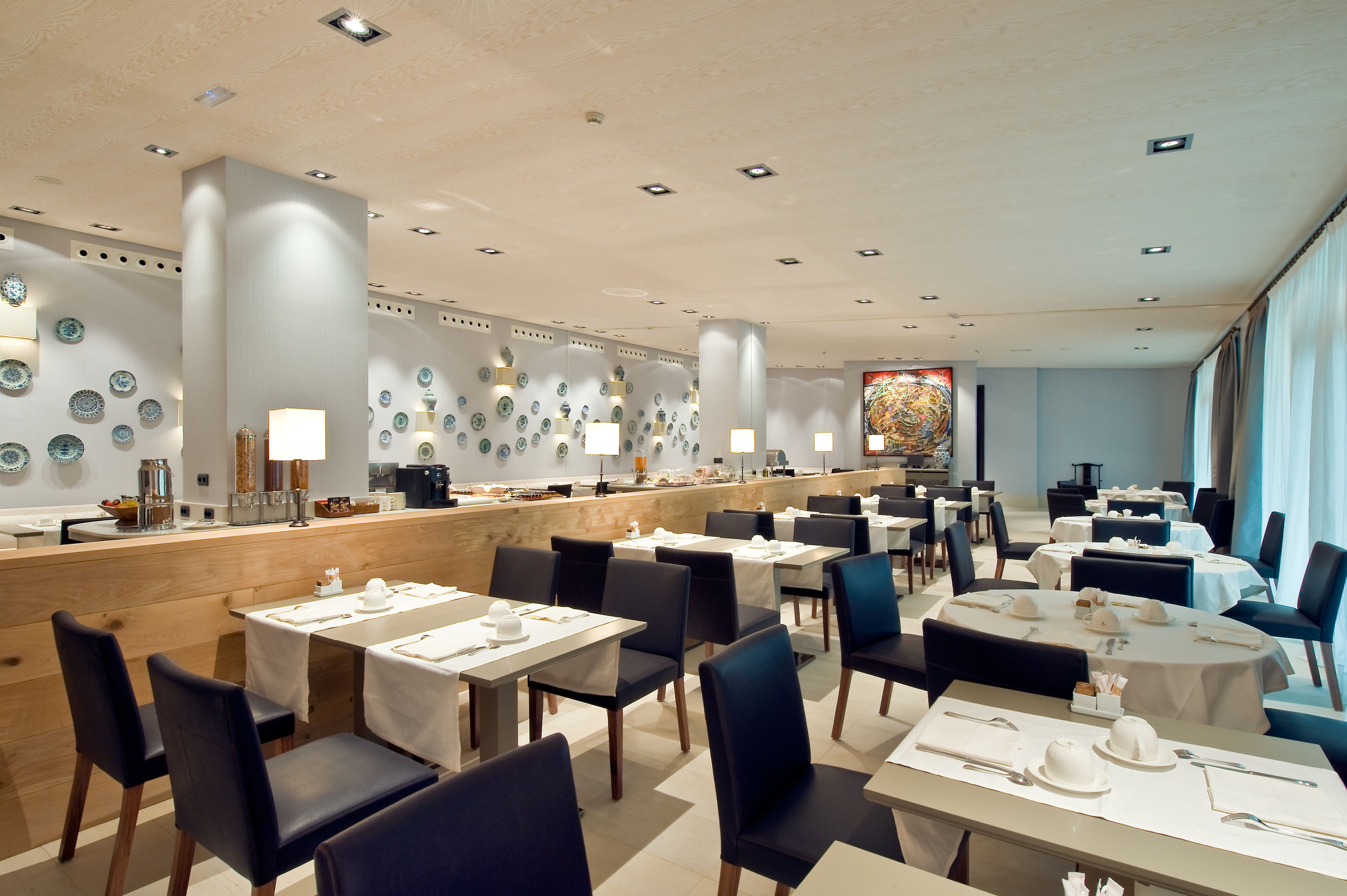 A restaurant with multiple tables and chairs, a counter with a coffee machine, and decorative plates on the walls.