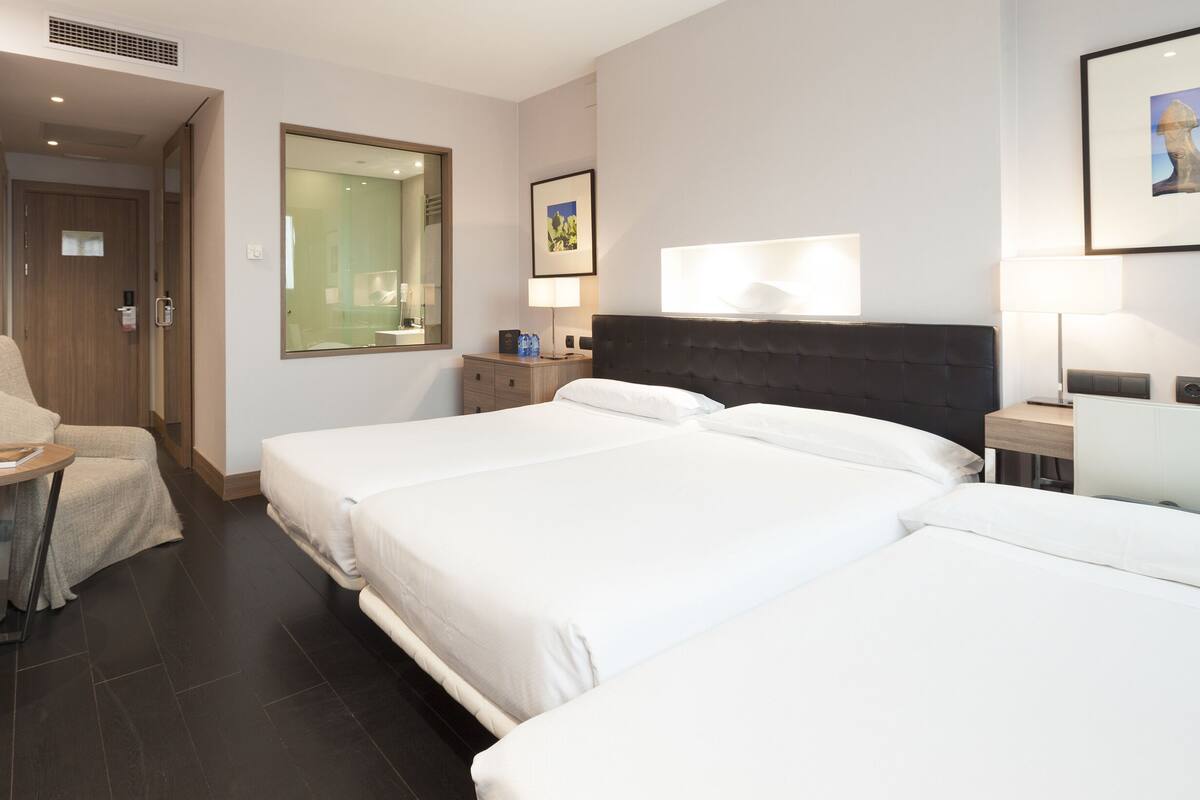 Ein Hotelzimmer mit zwei Betten, einem Schreibtisch mit Stuhl, einem Fernseher und einem Spiegel.