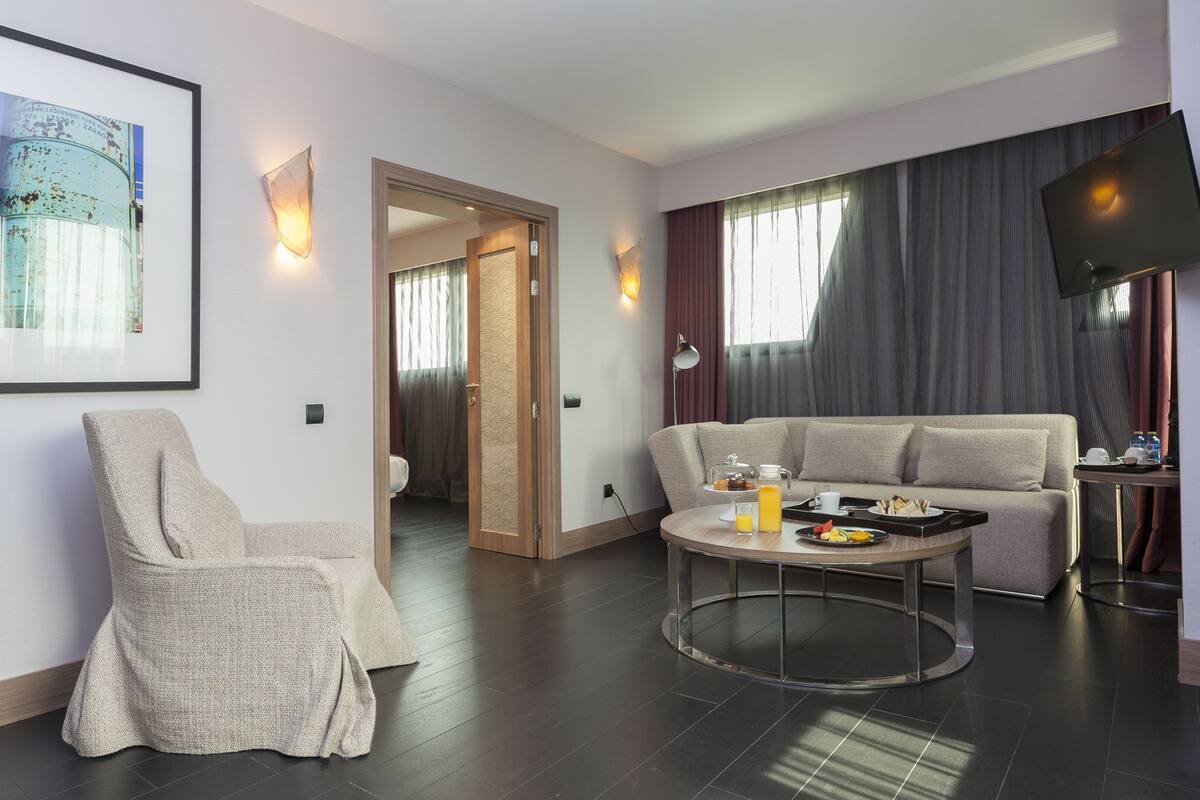 Ein modernes Hotelzimmer mit einem runden Esstisch, einer Couch, einem Sessel und einem Fernseher.