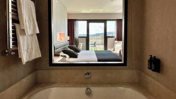 Un bagno d'hotel con una vasca da bagno ampia, un letto con vista sull'esterno e un portascopino.