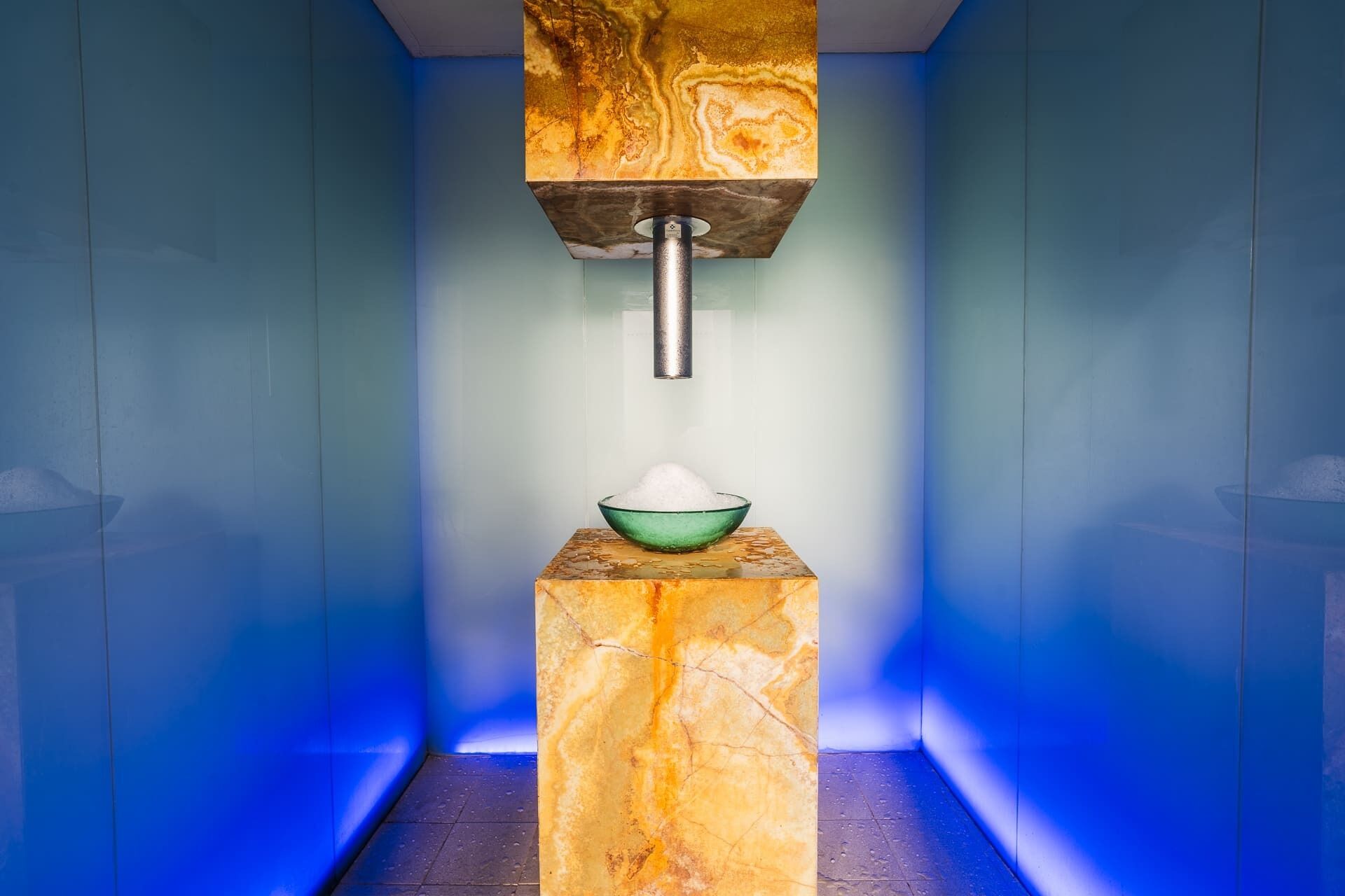 A bathroom with a marble sink, a green bowl, and a marble column.
