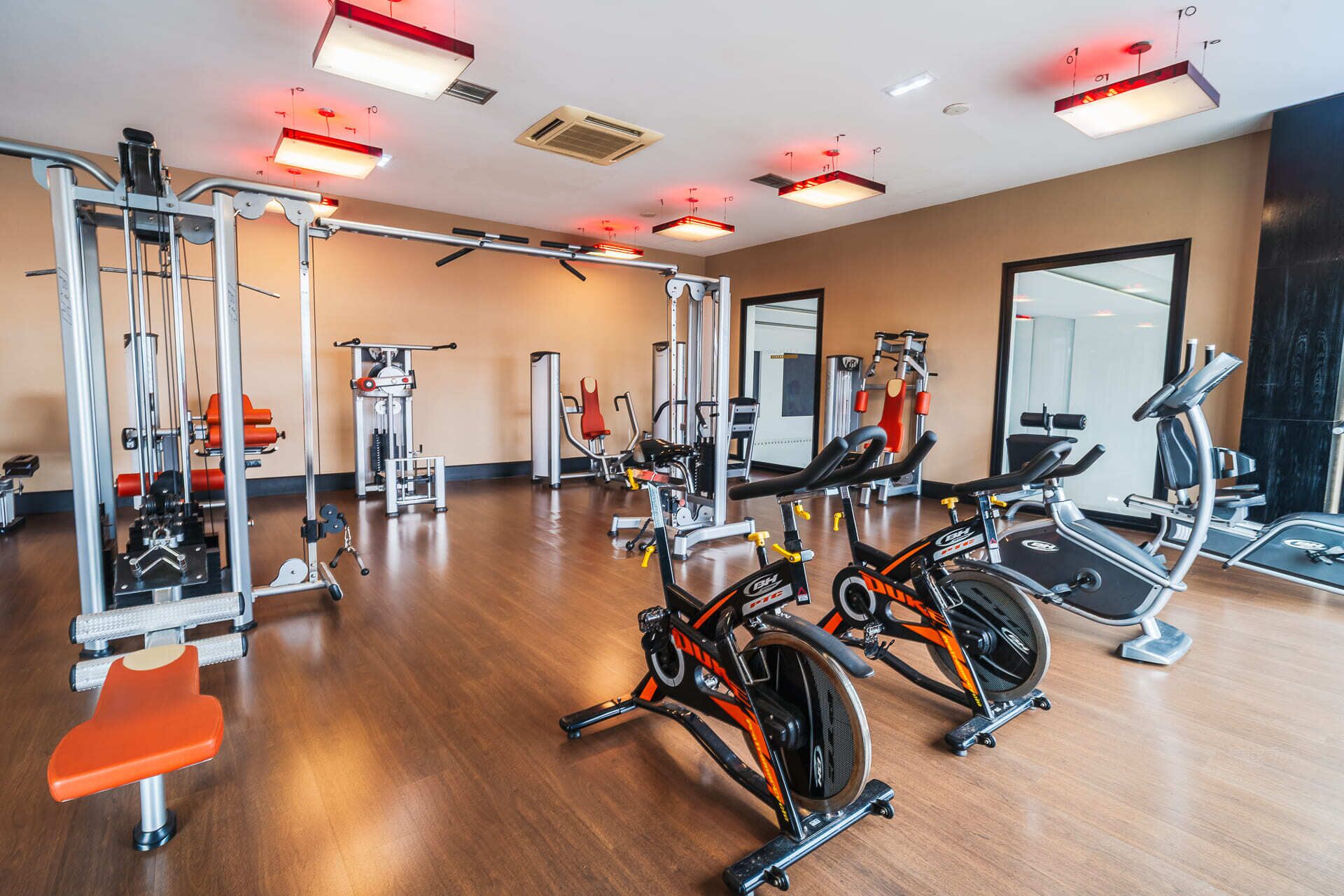 A gym with cardio machines, weight training equipment, and a mirror wall.