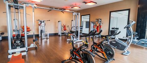 A gym with cardio machines, weight training equipment, and a mirror wall.