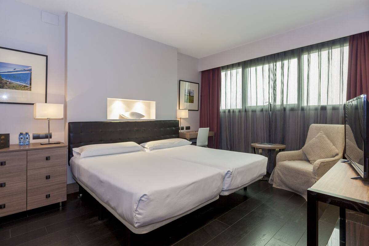 Ein Hotelzimmer mit einem großen Bett, einem Sessel, einem Schreibtisch und einem Fernseher.