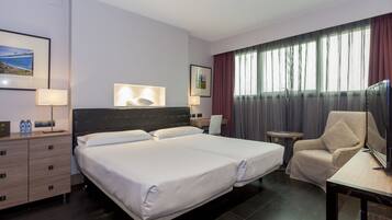 A hotel room with a large bed, a chair, a desk, and a TV.