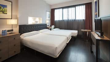 Una habitación de hotel con dos camas, un escritorio, una silla, un televisor y un ventanal con cortinas.
