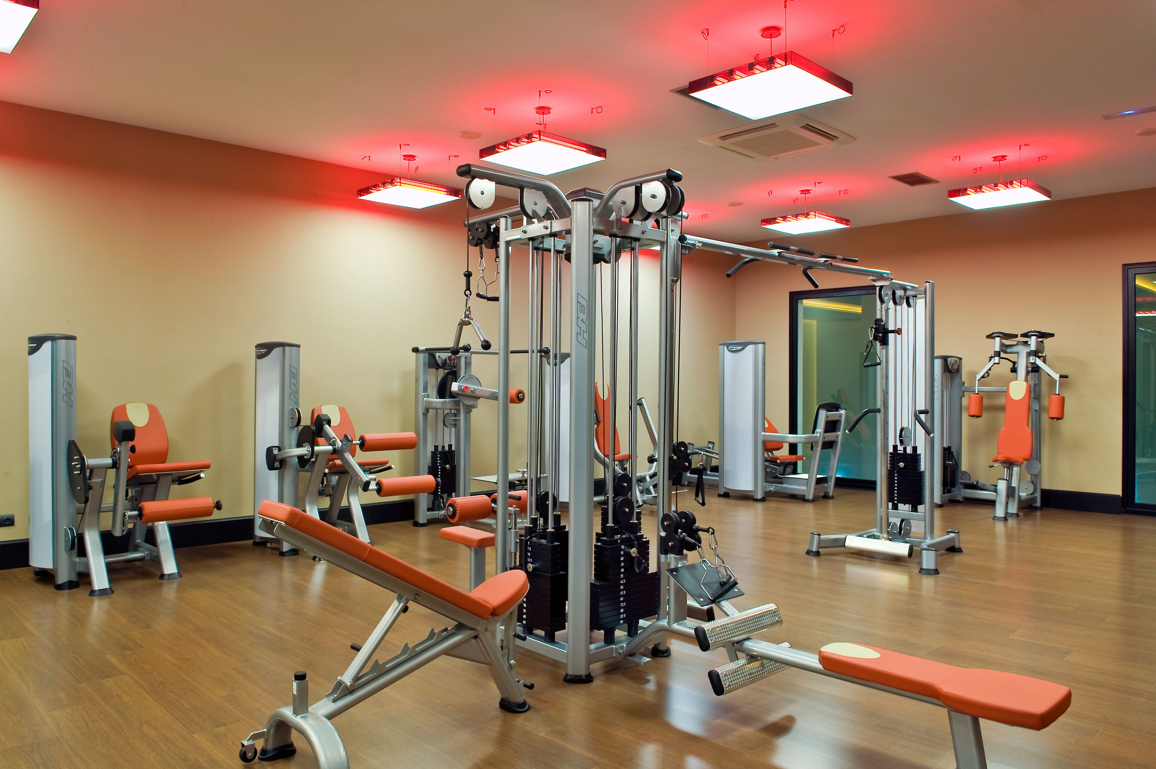 A gym with various exercise machines, mirrors, and red lighting.
