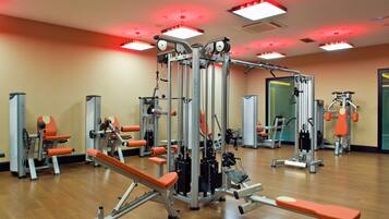 Un gimnasio con diversas máquinas de ejercicio, espejos e iluminación roja.