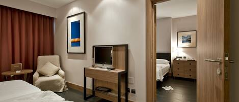 Habitación de hotel con cama, escritorio con computadora, silla, televisor y puerta que da a otra habitación.