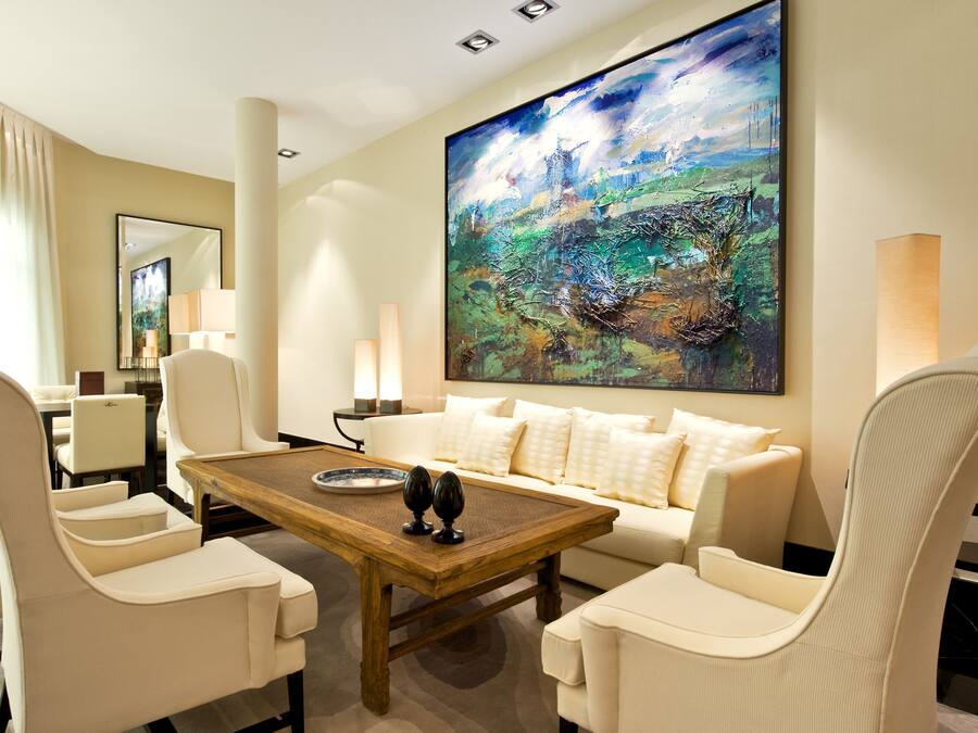 Een moderne woonkamer met een groot abstract schilderij, een beige bank en bijpassende fauteuils.