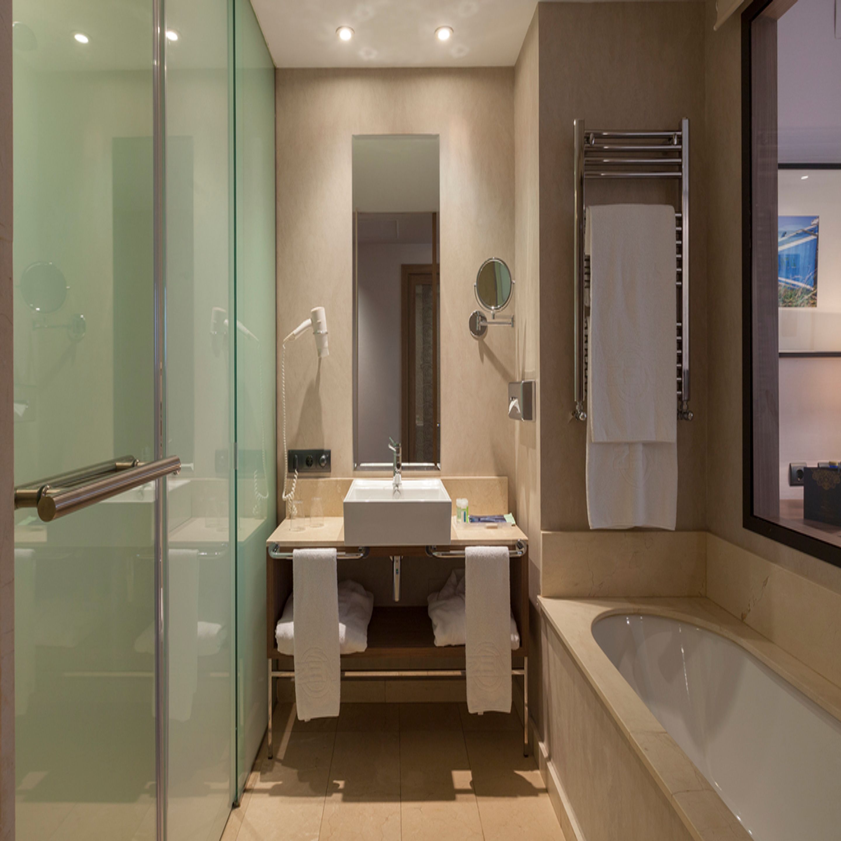 Une salle de bain moderne avec une douche à parois de verre, un lavabo avec un miroir, un porte-serviettes et une baignoire.