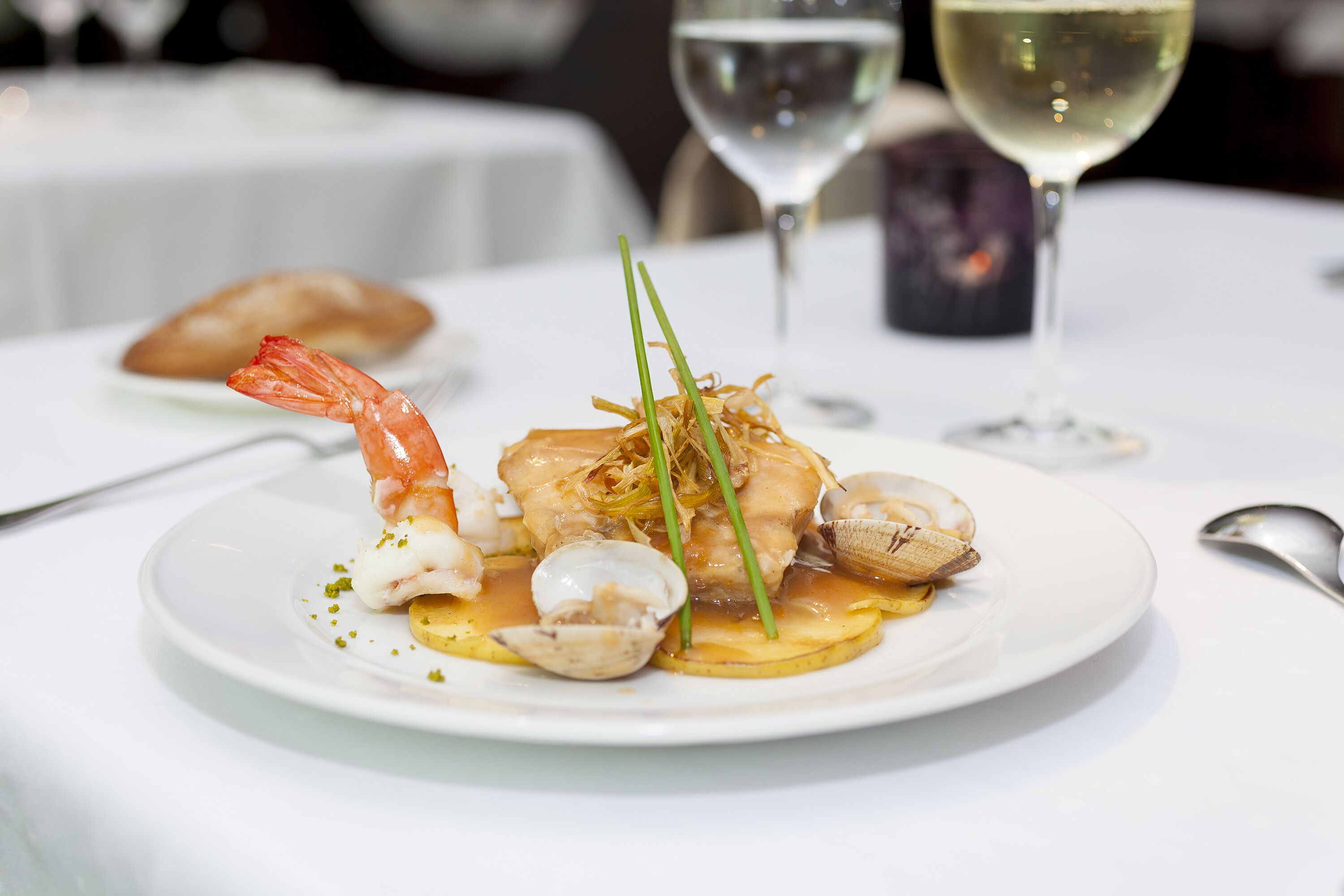 Un plato de mariscos sobre una vajilla blanca, acompañado de una copa de vino blanco y una vela al fondo.