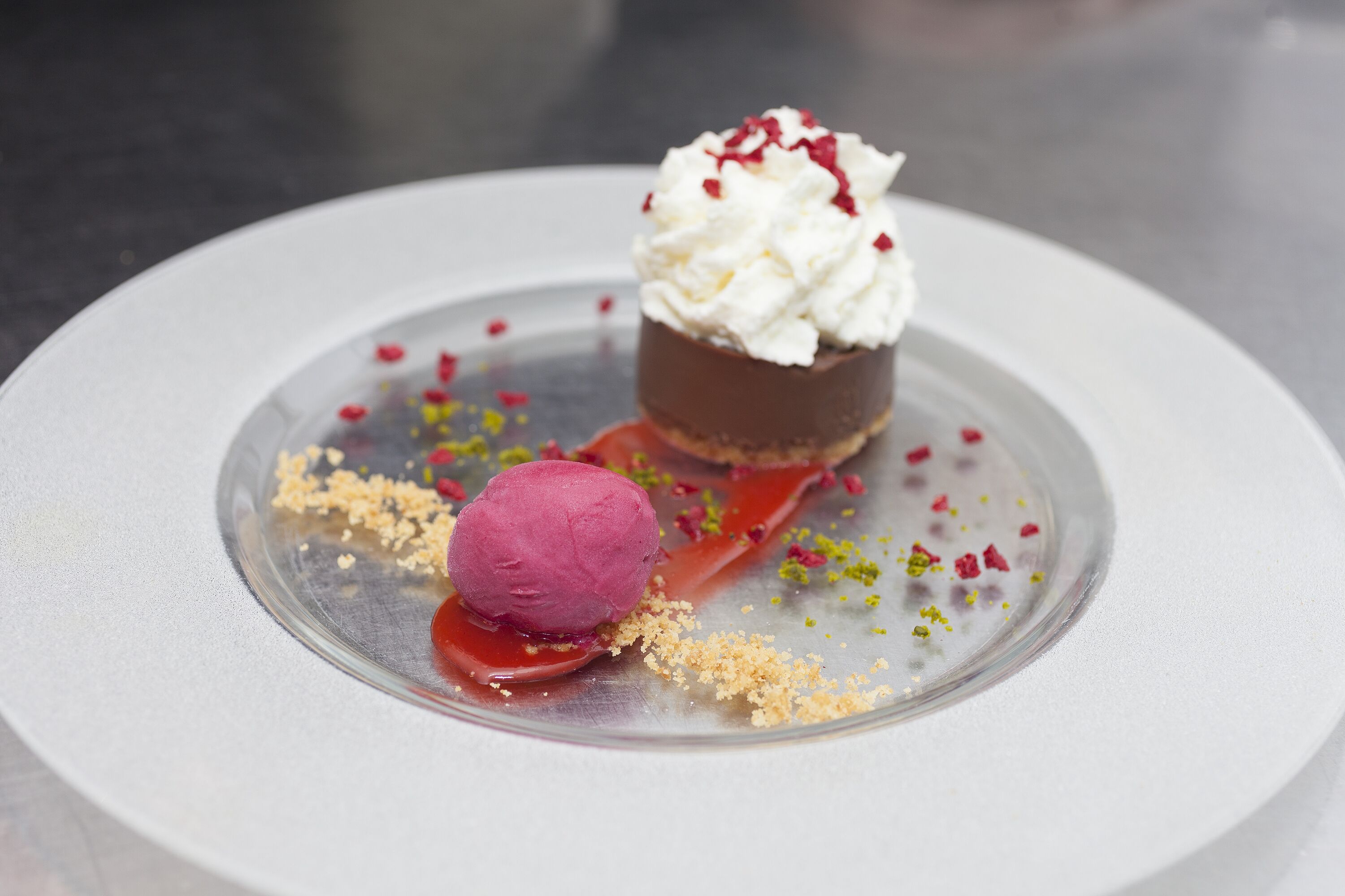 Un dessert composé d’une boule de glace et d’une sphère de chocolat, le tout présenté sur une assiette en verre transparent.