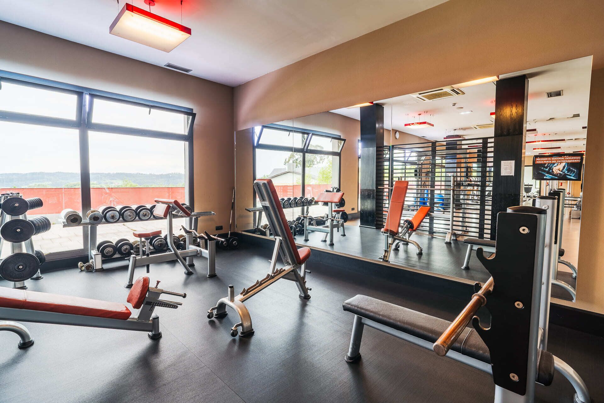 A gym with various exercise equipment, large windows, and a view of the outdoors.