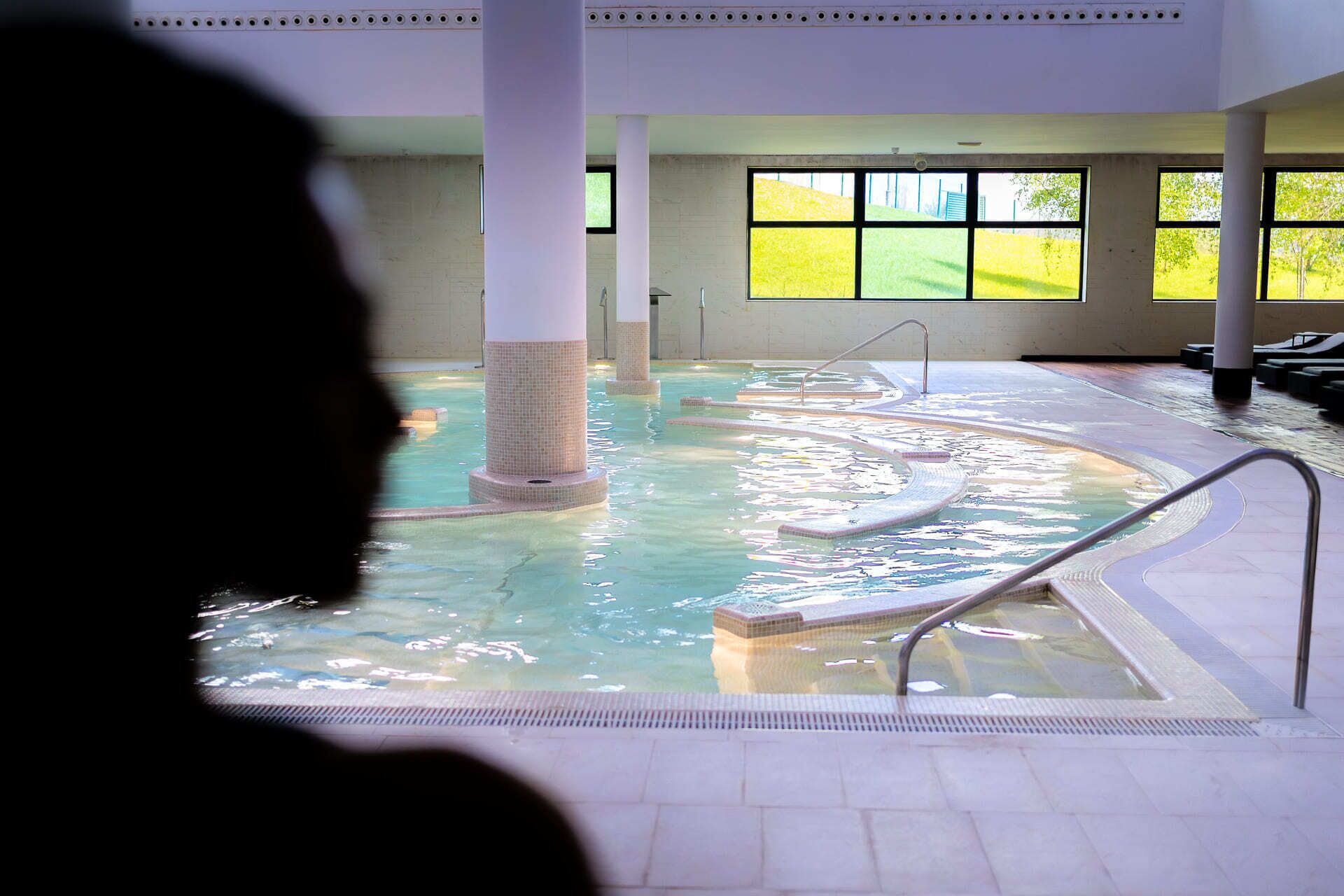 Une piscine intérieure à l’eau claire, avec des murs carrelés et de grandes fenêtres.