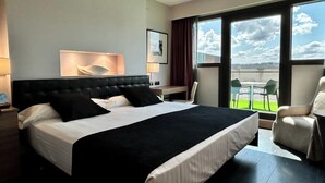 A modern hotel room with a large bed, a desk, and a view of the outdoors. - URH Hotel Zen Balagares (Corvera de Asturias)