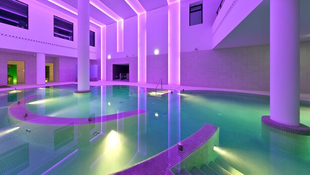 A large indoor swimming pool with a modern design, featuring a central island and multiple entry points. - URH Hotel Zen Balagares (Corvera de Asturias)