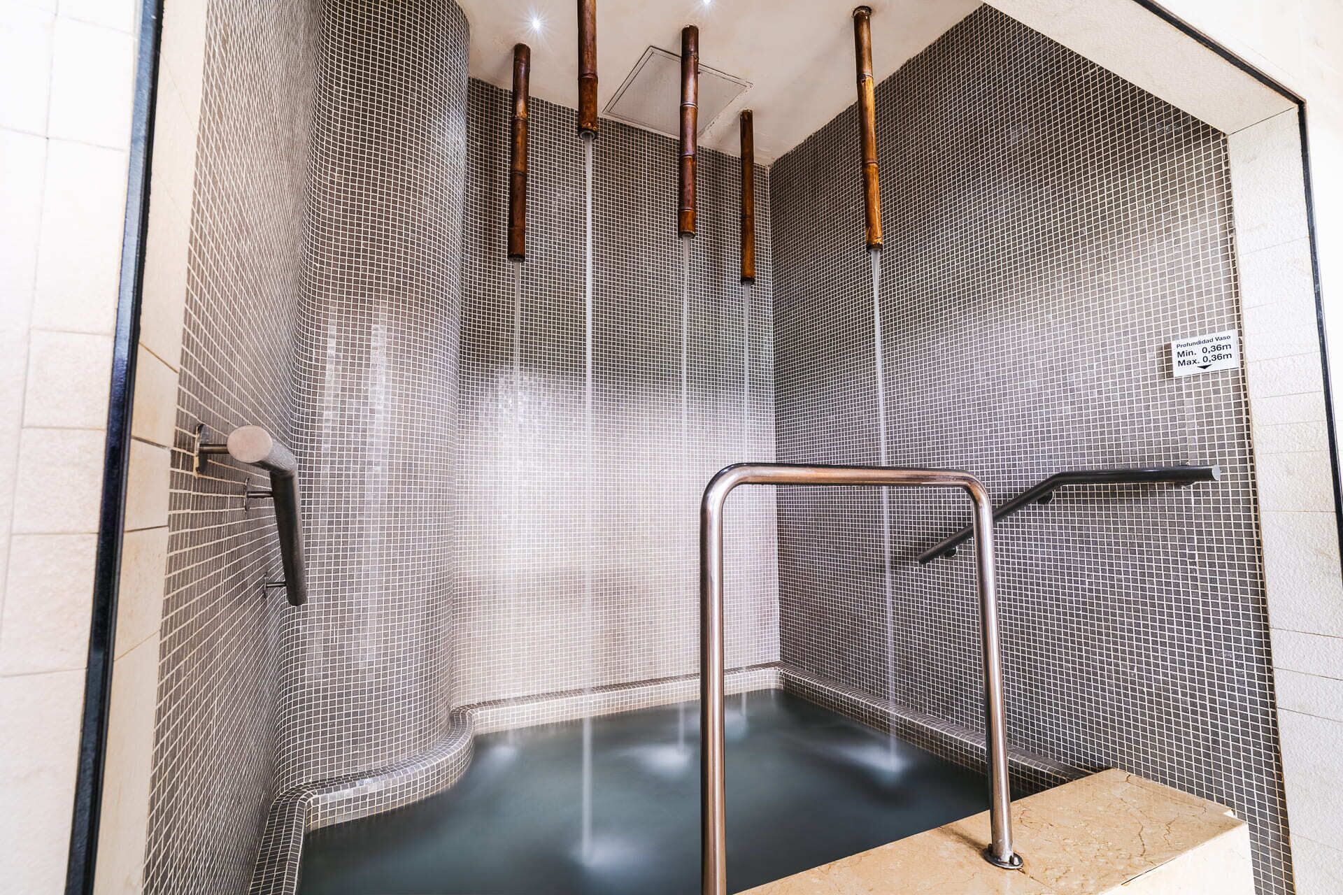 Un spa moderne avec un mur carrelé en noir et blanc, un banc en métal et un jacuzzi.