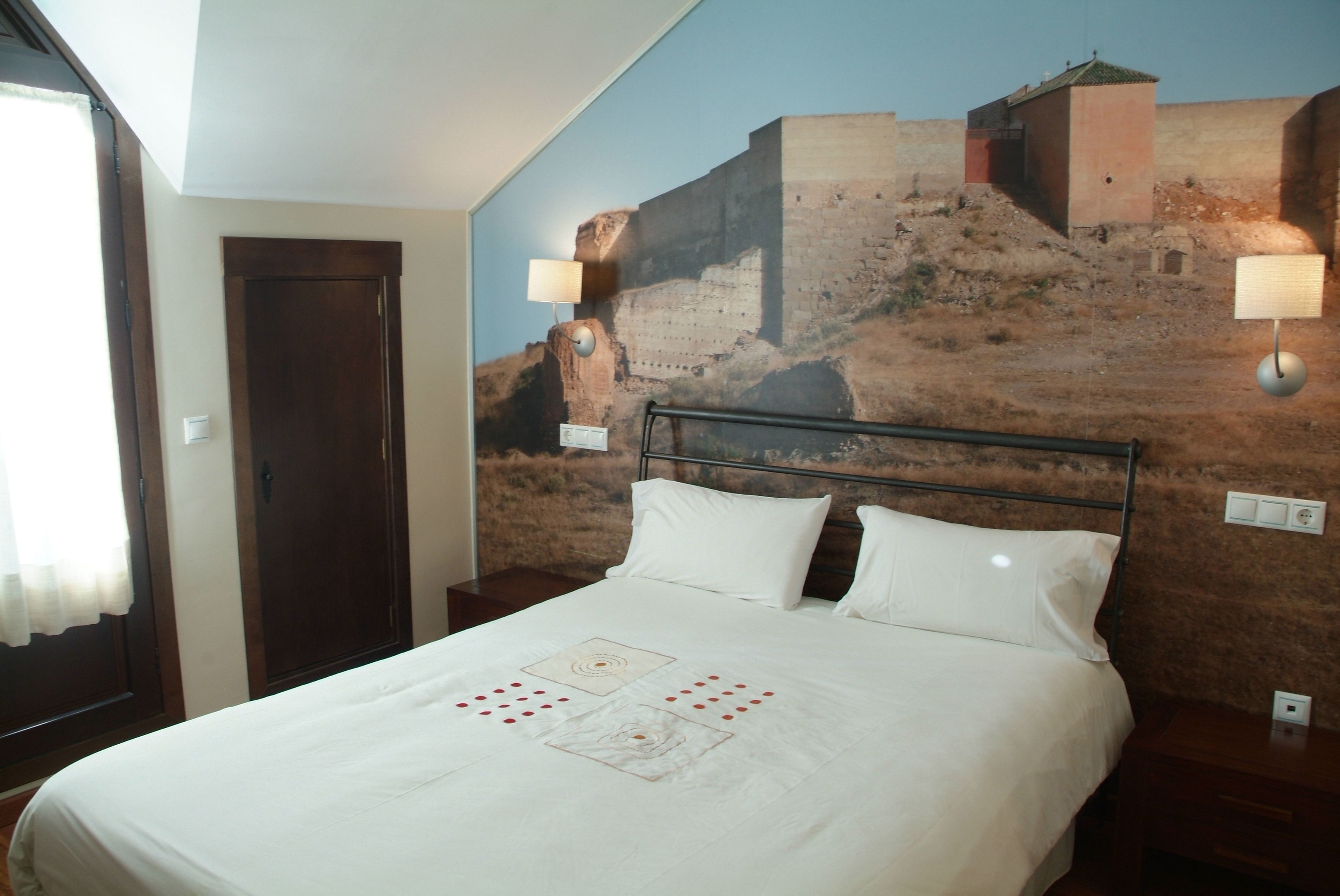 Een hotelkamer met een bed, een nachtkastje, een wandlamp en een deur.