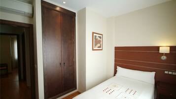 A hotel room with a large wooden wardrobe, a neatly made bed with a white bedspread, and a wall-mounted light fixture.