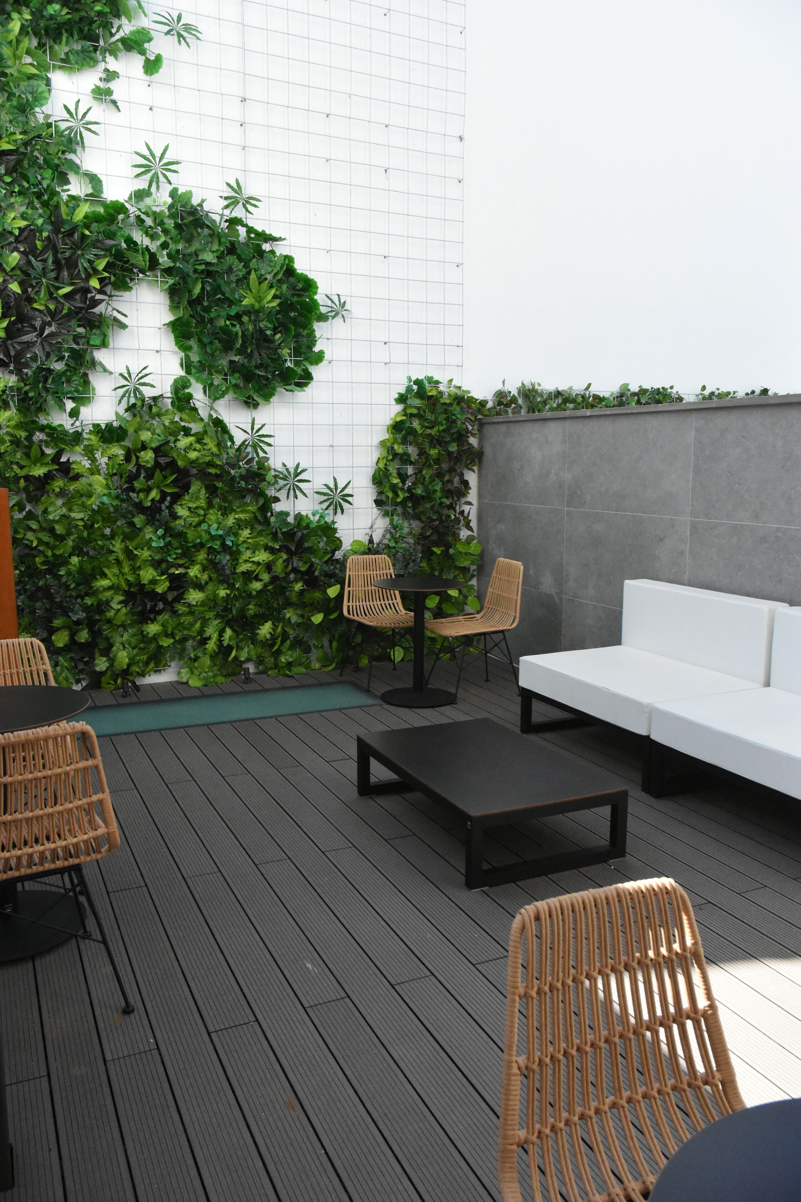 A modern outdoor seating area with a white sofa, wicker chairs, and a black coffee table on a wooden deck.