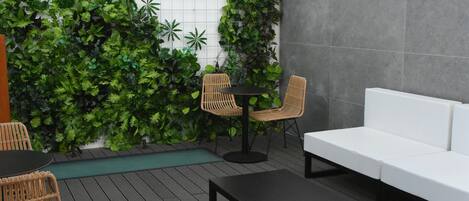 A modern outdoor seating area with a white sofa, wicker chairs, and a black coffee table on a wooden deck.