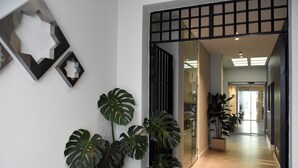 Un pasillo de diseño moderno, con una obra de arte geométrica en la pared y grandes plantas tropicales.