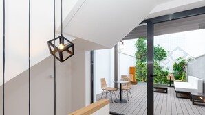 Un patio moderno al aire libre con suelo de madera, un comedor con sillas y una mesa, y una lámpara colgante.
