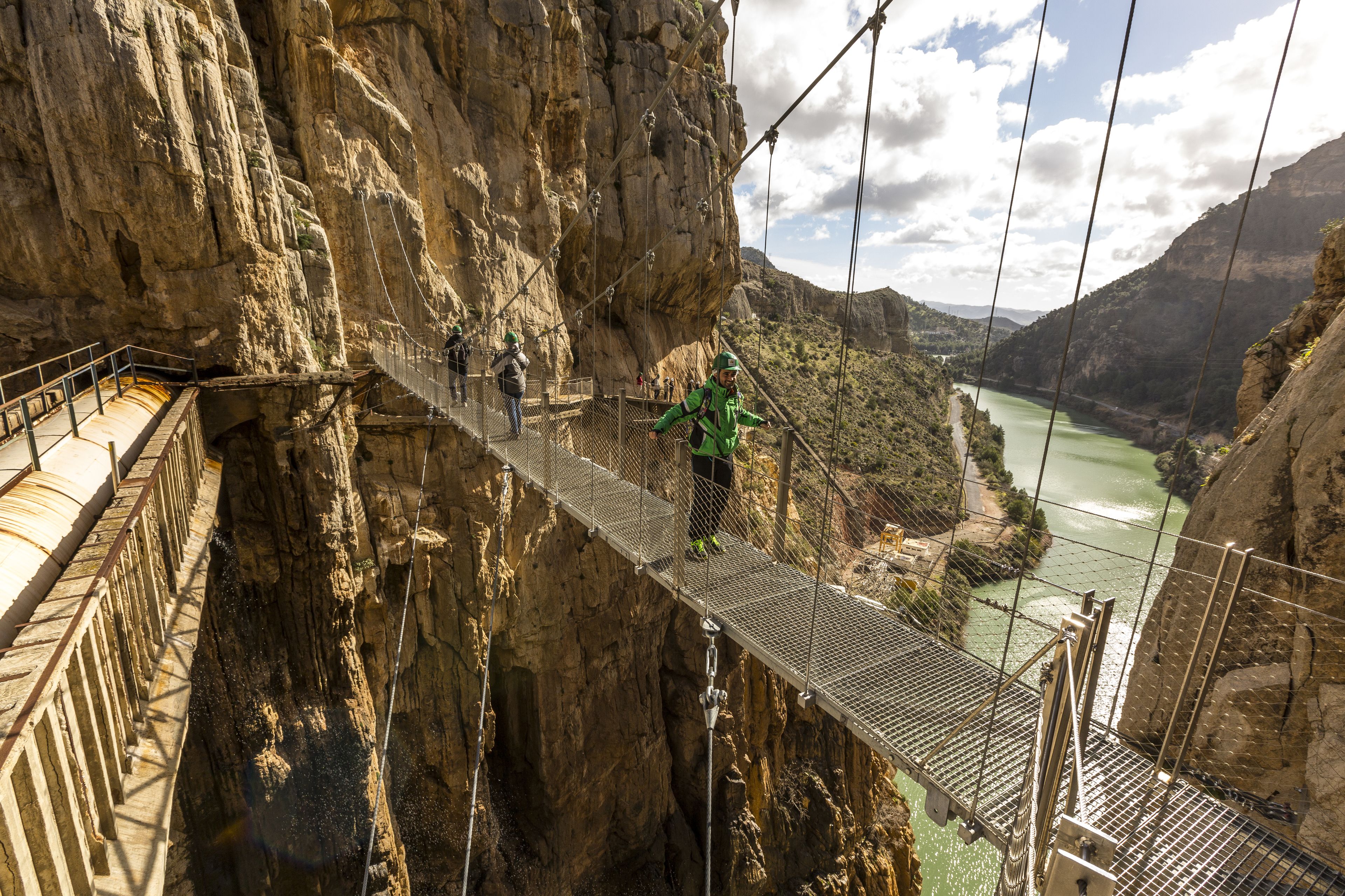 A suspension bridge with metal railings and a metal walkway, spanning a deep canyon with a river below.