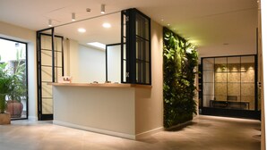 Zona de recepción con diseño moderno, que incluye un mostrador de recepción, un jardín vertical verde y un área de estar con una mesa y sillas.