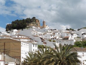 A coastal town with white buildings, a prominent church with a bell tower, and a rocky hill in the background. - Apartamentos Ardales (Ardales)