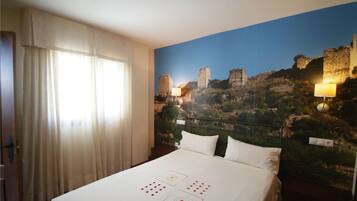 Habitación de hotel con cama, cortinas blancas, un mural de un sitio histórico y dos lámparas de pared.